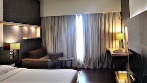 A hotel room with a bed, a sofa, a small round table, a TV, and a large window with curtains. - Hotel Satkar Residency (Thane)