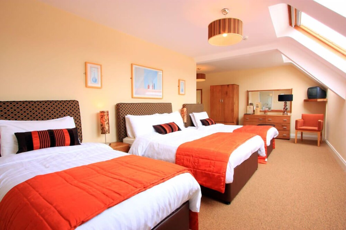 A hotel room with three beds, a desk, and a chair.