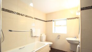 Ein Badezimmer mit Badewanne, Toilette und Waschbecken, mit Fliesenboden und -wänden.