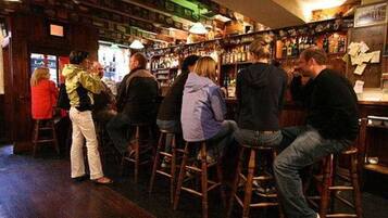 A bar with wooden stools and shelves stocked with bottles.
