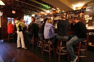 Un bar con taburetes de madera y estantes llenos de botellas.