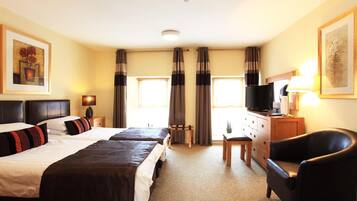 A hotel room with two beds, a desk with a television, a chair, and a window with curtains.