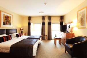 Habitación de hotel con dos camas, un escritorio con televisor, una silla y una ventana con cortinas.