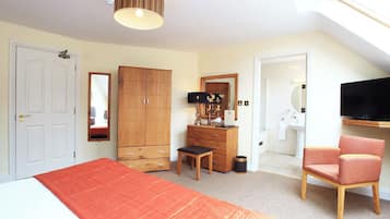 A bedroom with a bed, a wardrobe, a desk, a chair, a television, and a bathroom visible through an open door.