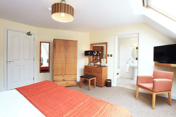 A bedroom with a bed, a wardrobe, a desk, a chair, a television, and a bathroom visible through an open door.
