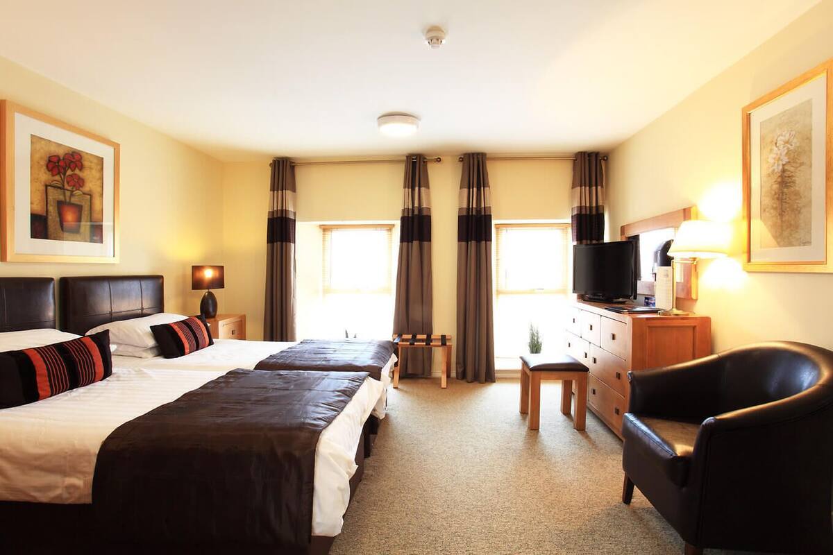 Ett hotellrum med två sängar, ett skrivbord med en tv, en stol och ett fönster med gardiner.