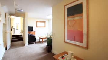 Habitación de hotel con pasillo alfombrado, un escritorio con cafetera, una silla, una planta y un cuadro en la pared.