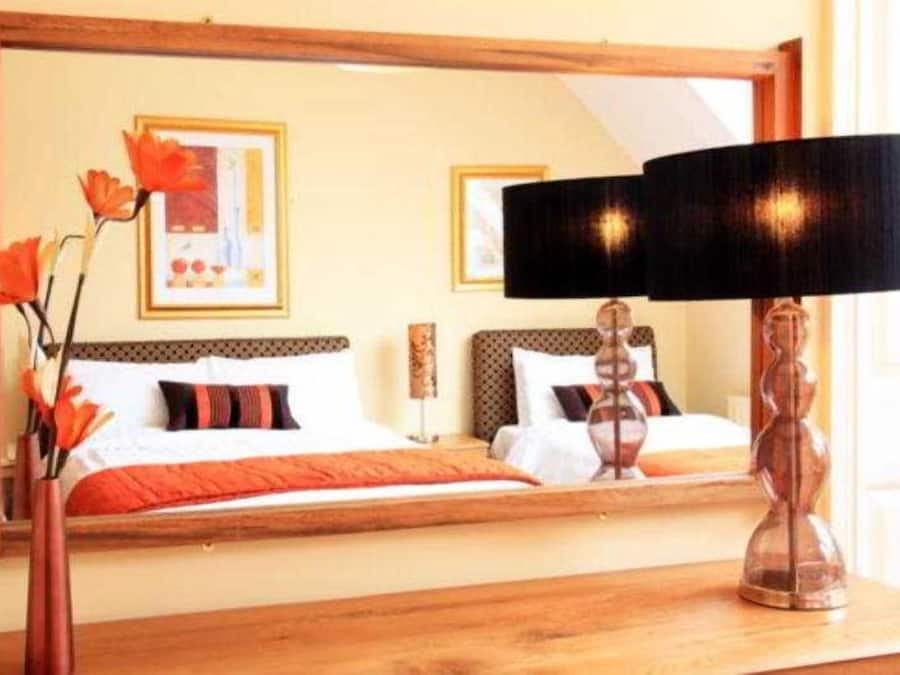 A hotel room with a bed, a mirror, a lamp, and a vase with flowers.