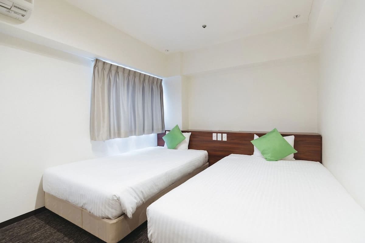 Habitació d'hotel amb dos llits individuals, una finestra amb cortines i aire condicionat al sostre.