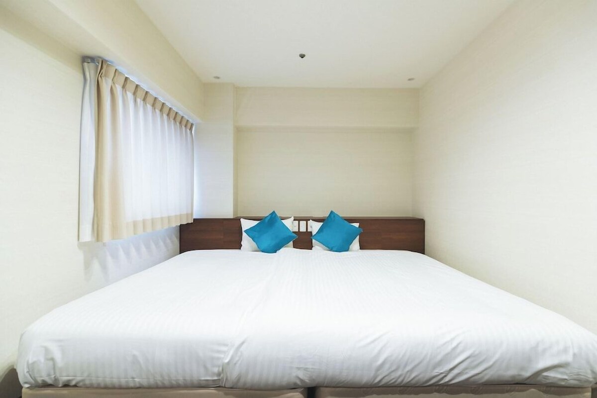 A single bed with a wooden headboard, white bedding, and two blue pillows.