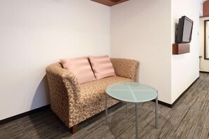 A room with a sofa, a small round table, and a television mounted on the wall. - Cityroute Hotel (Osaka)