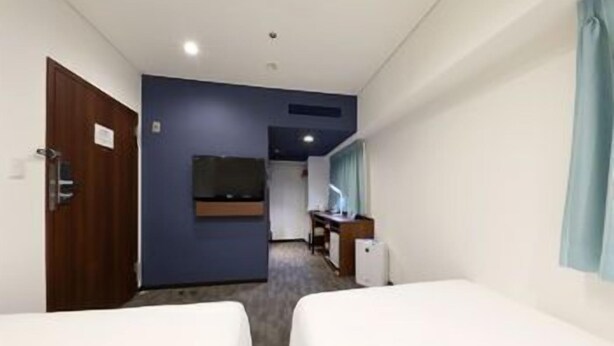 Hotellihuone, jossa on kaksi sänkyä, työpöytä, televisio ja ovi.