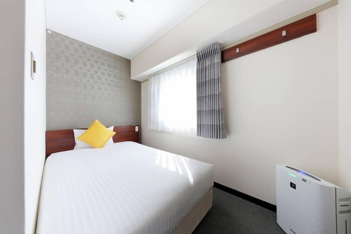 Habitació d'hotel amb un llit, una finestra amb cortines, aire condicionat fixat a la paret i un mur amb disseny.