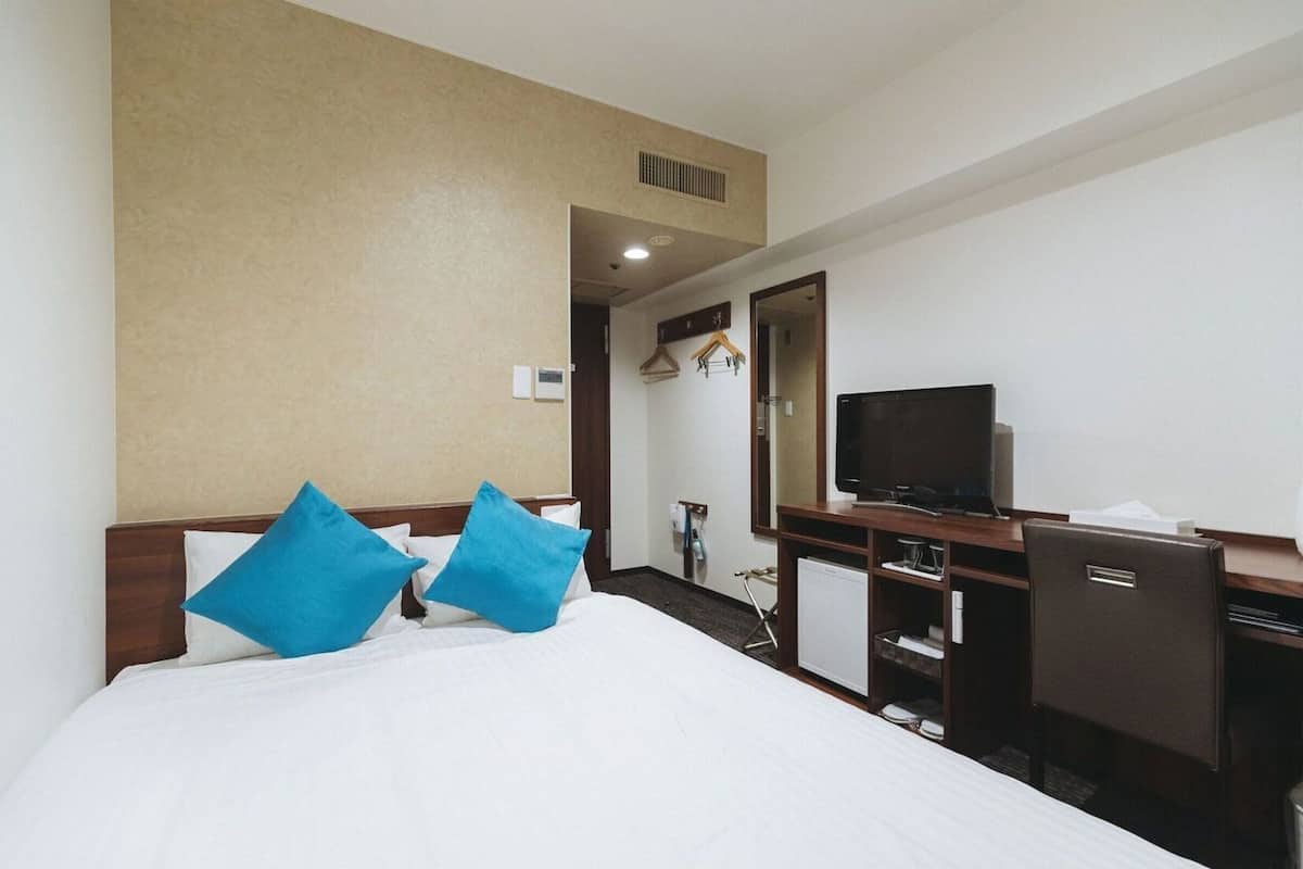 Habitació d'hotel amb un llit, un escriptori amb televisió, un mirall i una porta que condueix a una altra habitació.