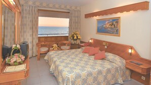 A hotel room with a large bed, a desk with a computer, a chair, and a view of the sea. - Rubi Hotel (Alanya)