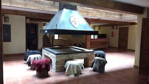 Ein rustikales Interieur mit Kamin aus Stein, Holzbalken und Fliesenboden.