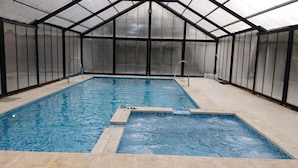Ein Innenpool mit klarem Wasser, umgeben von Glaswänden und einer Metall-Dachkonstruktion.