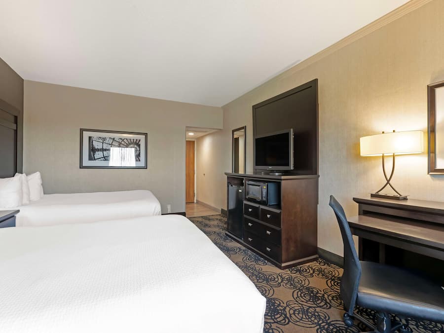 A hotel room with a large bed, a desk with a chair, a television, and a desk lamp.