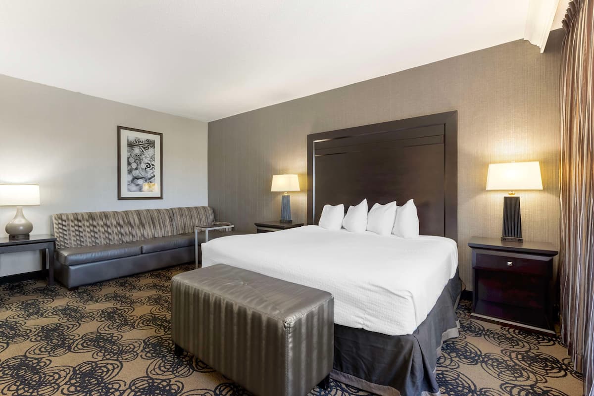 A hotel room with a large bed, a sofa, an ottoman, two nightstands, and a wall-mounted lamp.