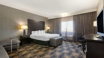 Quarto de hotel com cama, mesas de cabeceira, escrivaninha, cadeira e televisão.