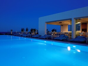 A modern pool area with lounge chairs and a dining area, overlooking a body of water.