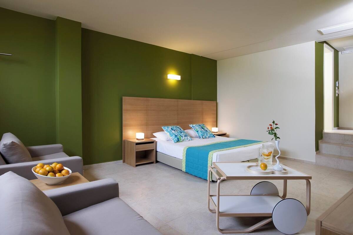 A hotel room with a bed, bedside tables, a small table with a drink, and a sofa.