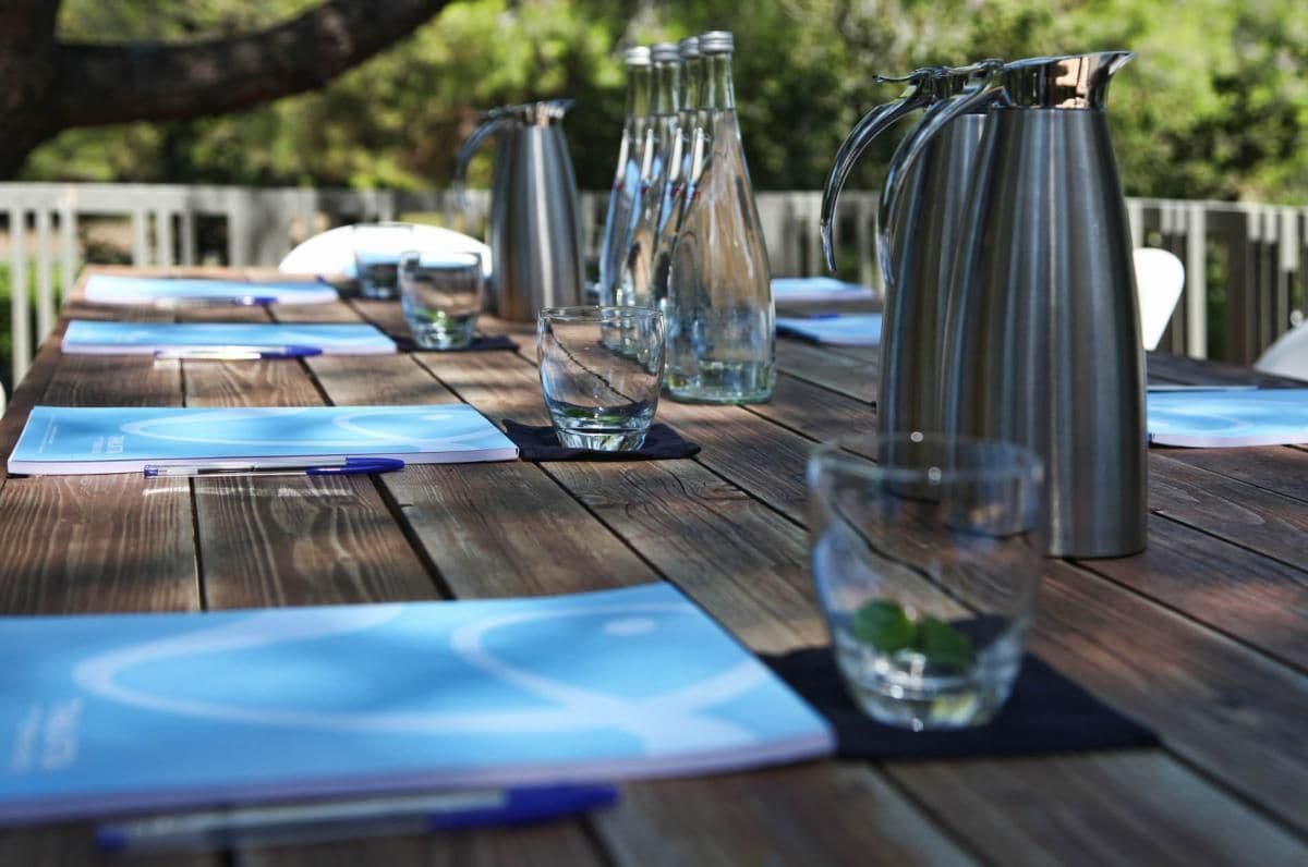 A wooden table with metal pitchers, glasses, and notepads.