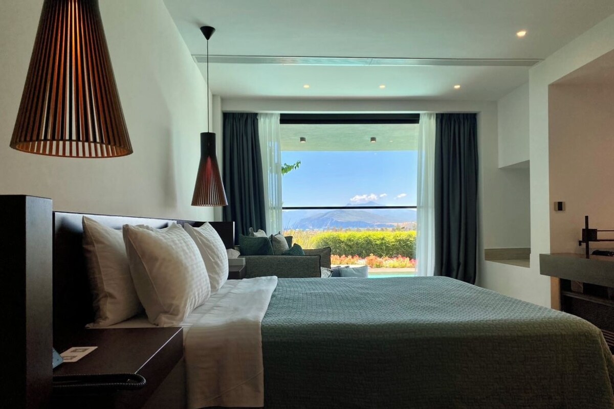 A modern hotel room with a large bed, a desk, and a view of the outdoors.