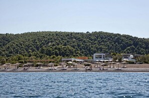 A beach resort with beach umbrellas, sun loungers, and a view of a forested hill. - Thalatta Seaside Hotel (Mantoudi-Limni-Agia Anna)