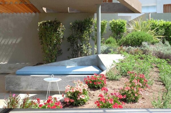 A modern outdoor seating area with a bench, a small table, and various plants.
