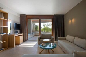 A modern hotel room with a sofa, a small round table with a tray of items, a TV, and a bookshelf.