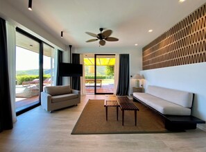 A modern living room with a sofa, a coffee table, and a TV. There is a sliding glass door leading to an outdoor area. - Thalatta Seaside Hotel (Mantoudi-Limni-Agia Anna)