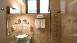 Une salle de bain moderne dotée d’une douche à parois de verre, d’un grand miroir, d’un lavabo avec un plan de toilette en verre et d’un porte-serviettes.