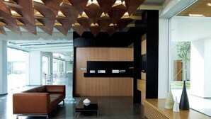 Un espace d’accueil moderne, avec un comptoir de réception en bois, un canapé en cuir et une grande fenêtre offrant une vue sur l’extérieur.