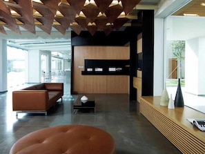 A modern reception area with a wooden reception desk, a leather sofa, and a large window providing a view of the outdoors. - Thalatta Seaside Hotel (Mantoudi-Limni-Agia Anna)
