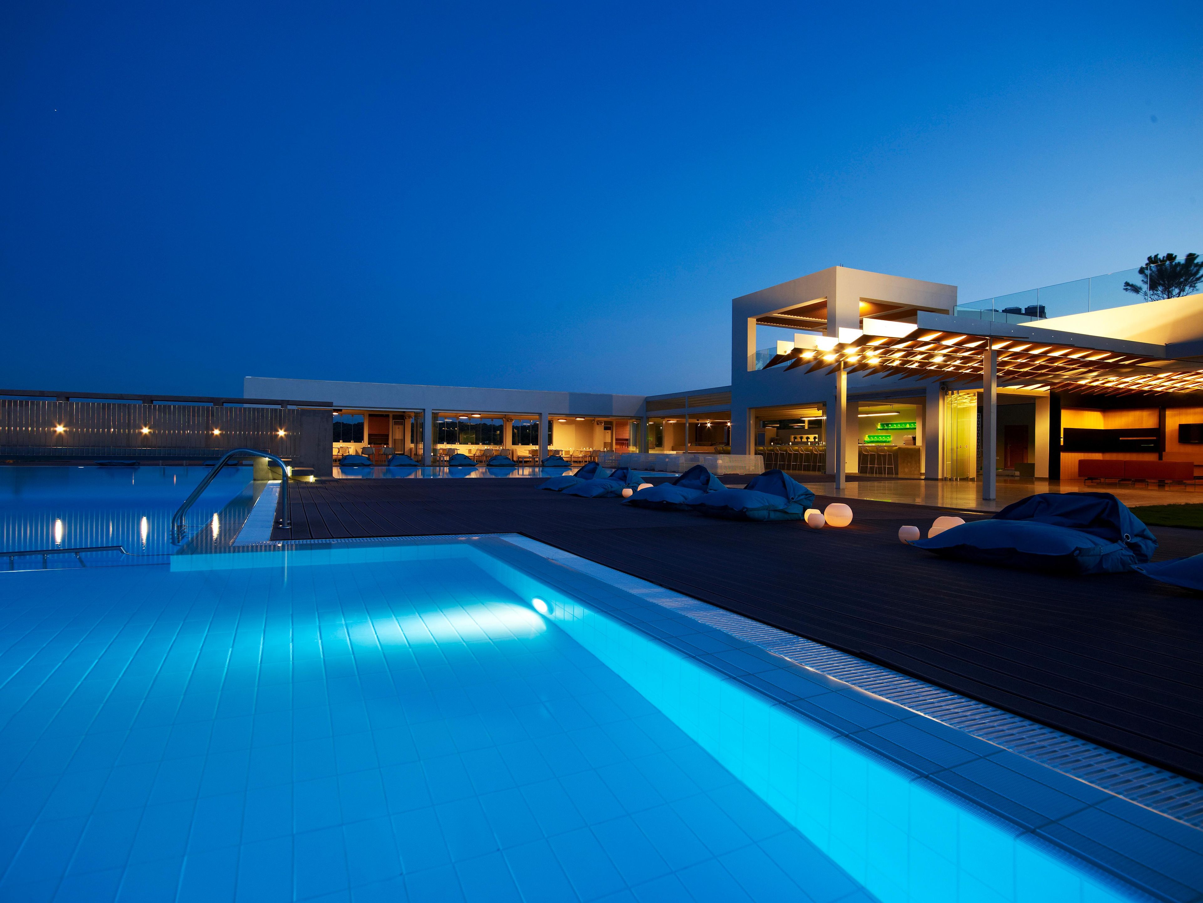 Un hotel moderno con piscina, asientos al aire libre y un área techada con luces.
