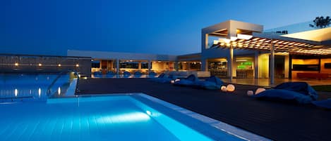 Un hotel moderno con piscina, asientos al aire libre y un área techada con luces.
