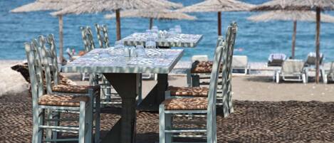 A beachside restaurant with tables and chairs, umbrellas, and a view of the ocean.