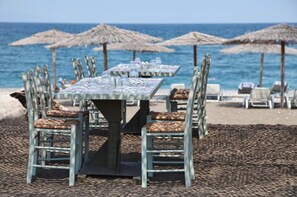 A beachside restaurant with tables and chairs, umbrellas, and a view of the ocean. - Thalatta Seaside Hotel (Mantoudi-Limni-Agia Anna)