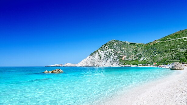 A beach with clear turquoise water, white sandy shore, and a rocky hill with greenery. - Niforos Panorama (Kefalonia)
