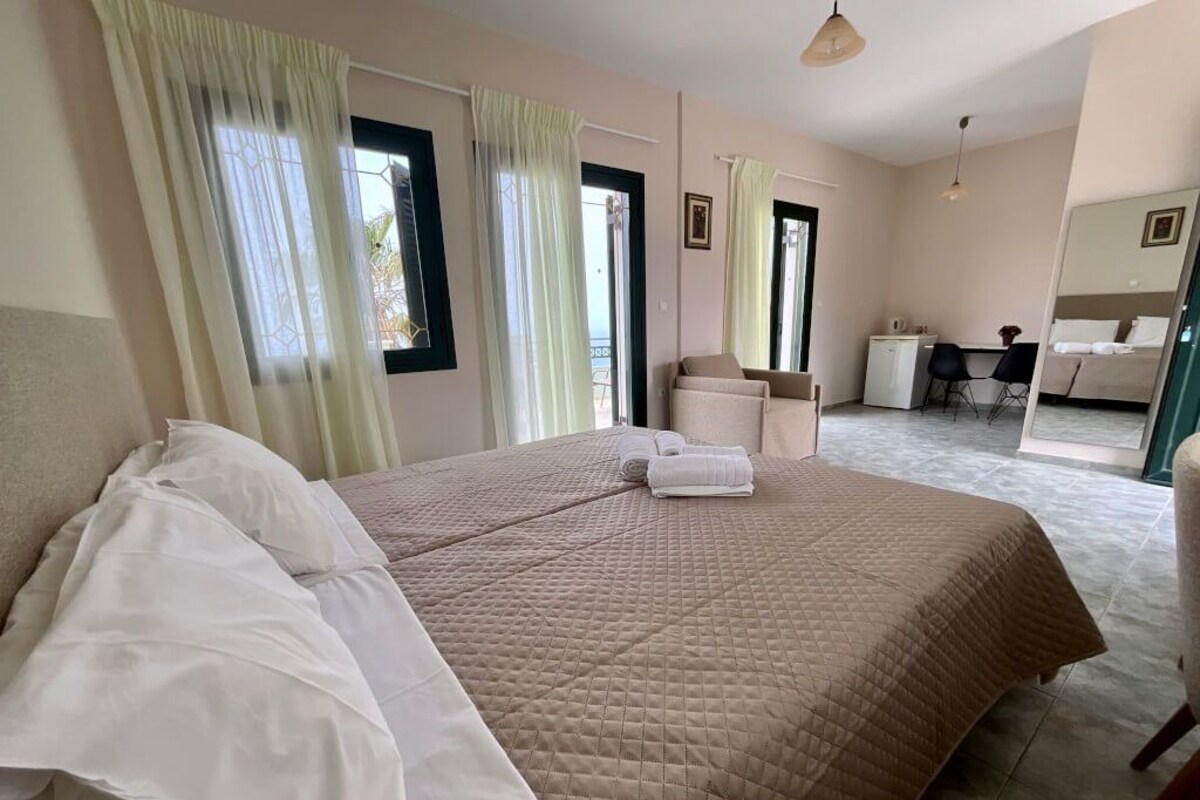 A bedroom with a large bed, a desk, a chair, and a mirror.