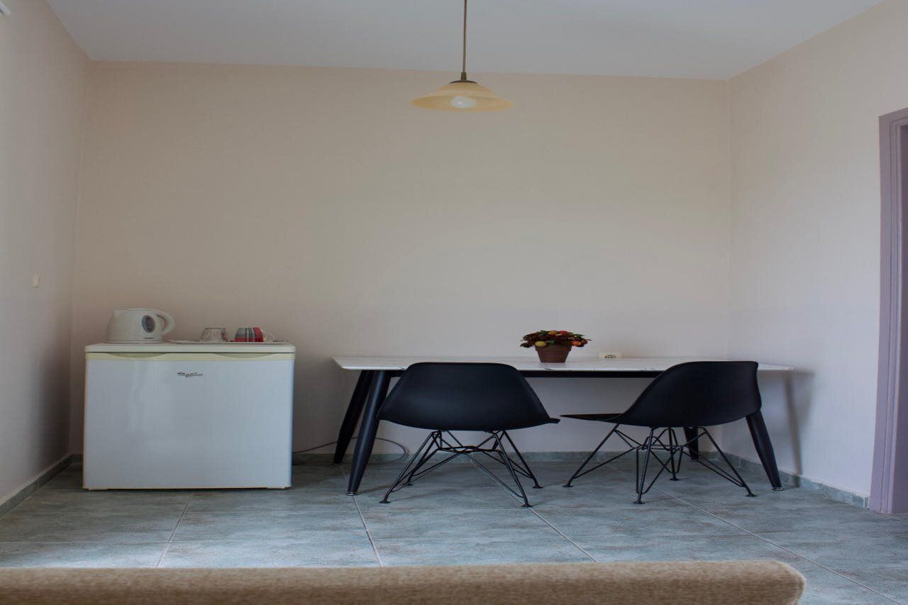 A compact kitchen with a white refrigerator, a white table, two black chairs, and a hanging light fixture.