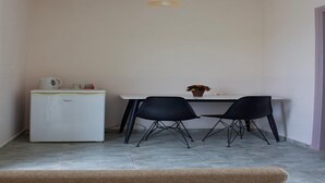 A compact kitchen with a white refrigerator, a white table, two black chairs, and a hanging light fixture. - Niforos Panorama (Kefalonia)