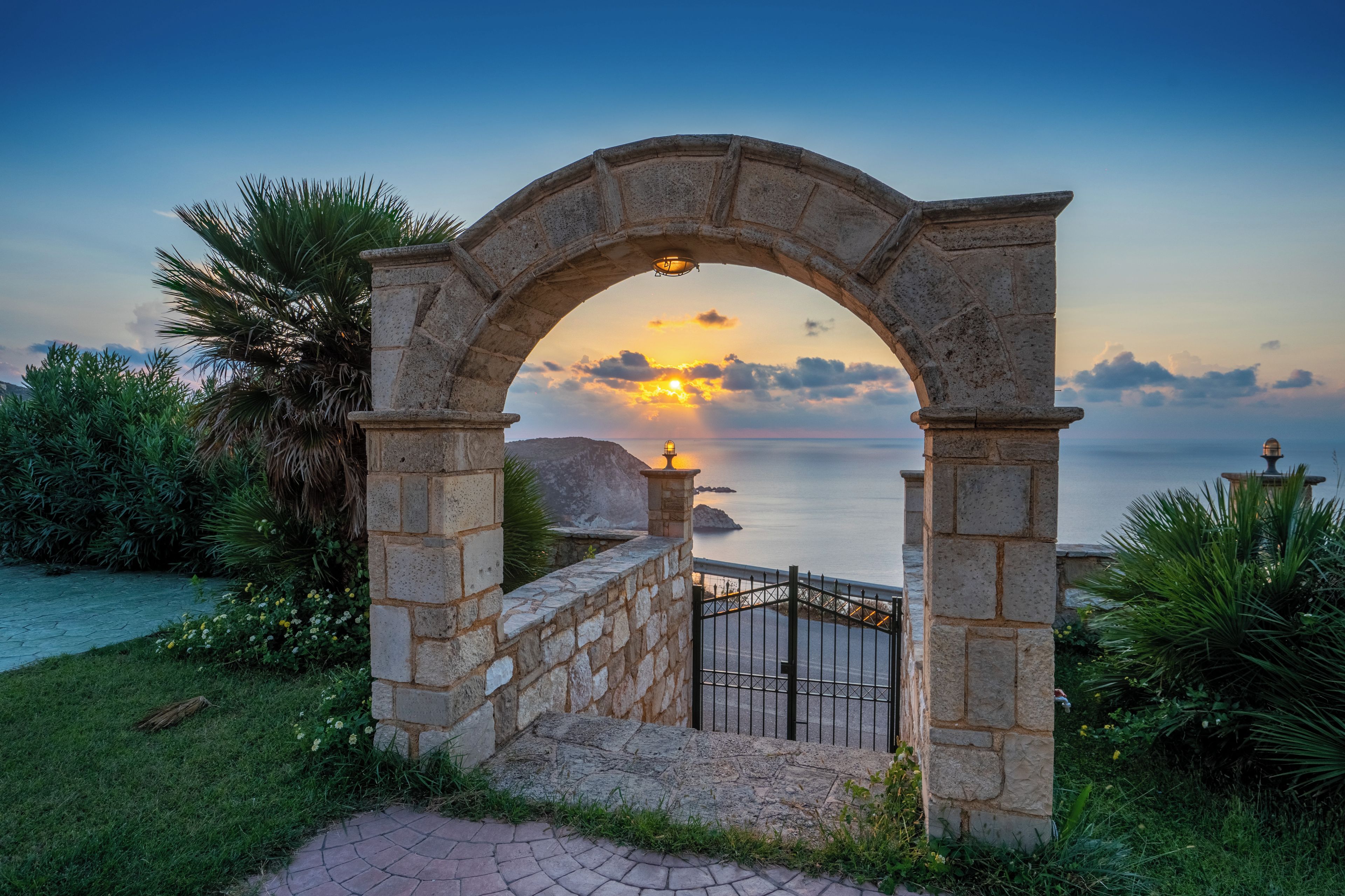 A stone archway leading to a coastal view with a sunset.