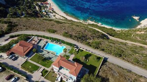 An aerial view of a coastal property with a swimming pool, a road, and a beach. - Niforos Panorama (Kefalonia)