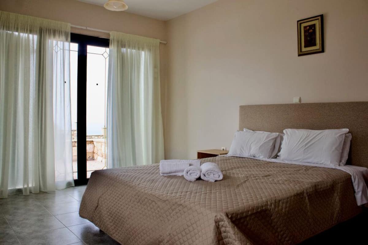 Quarto de hotel com cama, cortinas, um quadro na parede e vista pela janela.
