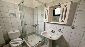 A bathroom with a glass-enclosed shower, a toilet, and a sink with a mirror above it. - Niforos Panorama (Kefalonia)