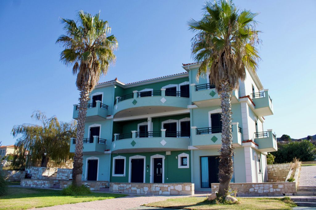 A multi-story building with balconies, a stone facade, and palm trees.