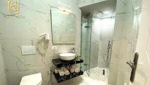 Un baño moderno con inodoro blanco, tocador negro con lavamanos blanco, cabina de ducha de cristal y salpicadero de mármol.