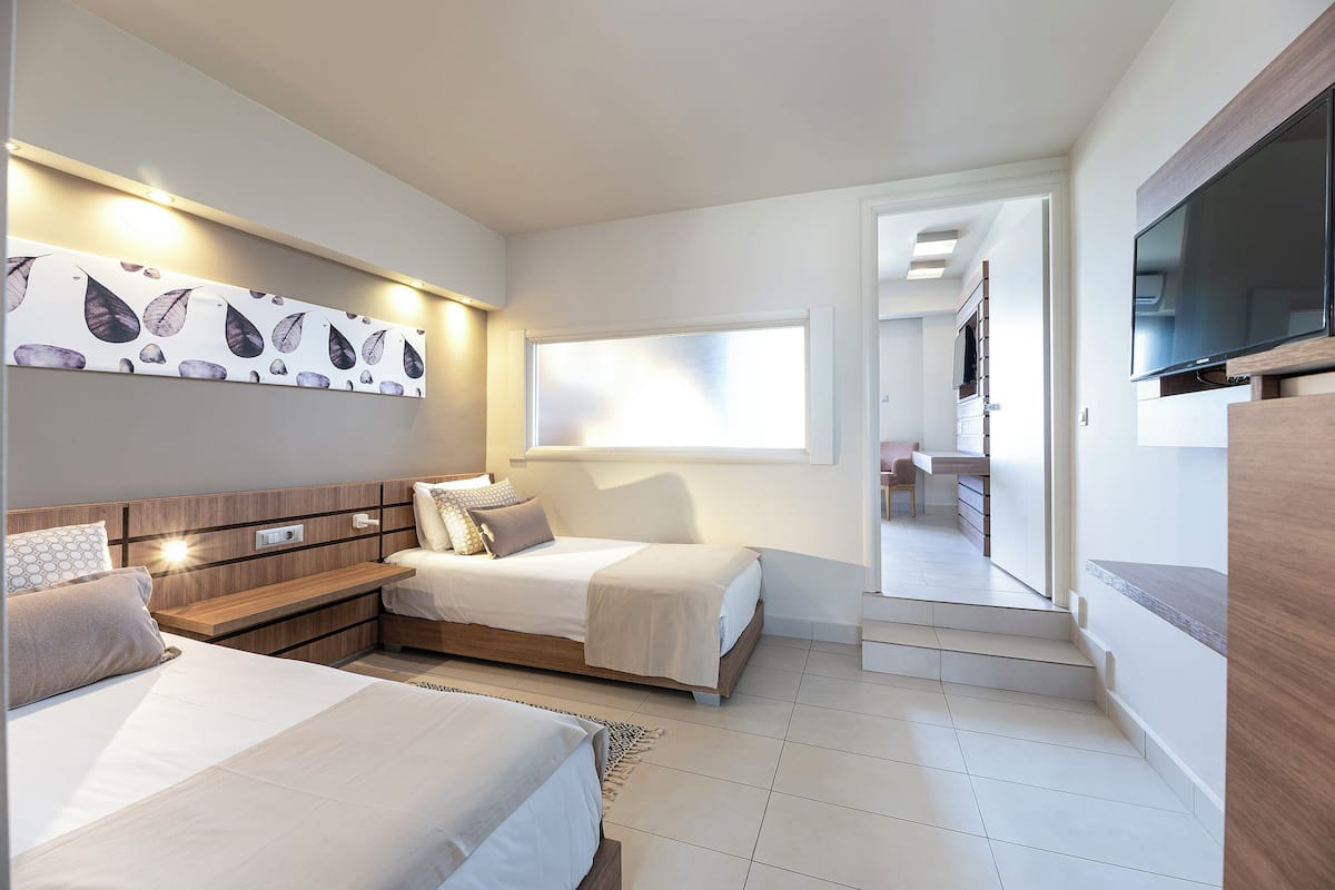 A modern hotel room with two beds, a flat-screen TV, a large window, and a view of the hallway.